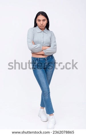 A serious asian woman with mid-length straight hair in a long sleeved cutoff blouse and blue jeans. Possible college student. Isolated on a white backdrop.