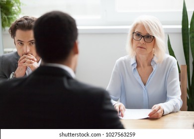 Serious attentive senior female hr manager employer listening to candidate at job interview, focused strict mature businesswoman thinking about hiring decision at difficult group negotiations concept - Shutterstock ID 1027563259