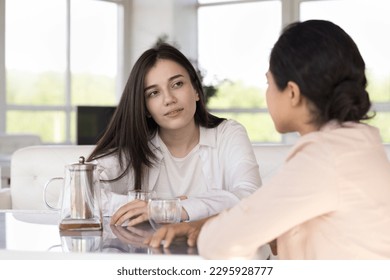 Serious attentive woman spend time with Indian female friend listen her, sit together at table with teapot, having reliable talk meet in cafe. Friendship, relations, honest trustworthy conversation - Powered by Shutterstock