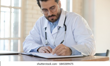 Serious Attentive Young Male Doctor Qualified Specialist Surgeon Therapist Focused On Filling Patient Chart, Thinking On Diagnosis Definition In Records, Studying Materials To Write Scientific Article