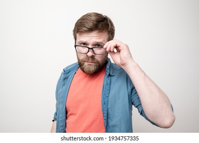 Ein seriöser, attraktiver Mann schaut sich die Kamera streng an und hält eine Brille mit Händen. Weißer Hintergrund.