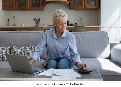 Serious Attractive Mature Woman Sit On Sofa Calculates Expenses On Calculator, Use Laptop Paying Bills Through E-bank App At Home. Family Budget Control, Financial Management, Accounting Job At Home