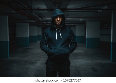 Serious attractive muscular caucasian sportsman in hoodie standing in underground garage with hands in pockets at night. Urban life concept. - Powered by Shutterstock