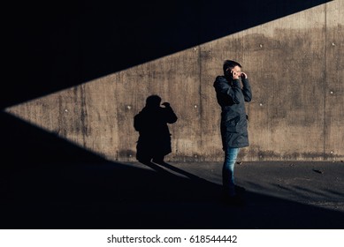 Serious Authentic Woman With Short Hair Talking On Mobile Phone On The Street In The Under Passage, Winter Setting Sun Casting Contrasty Shadows On The Wall