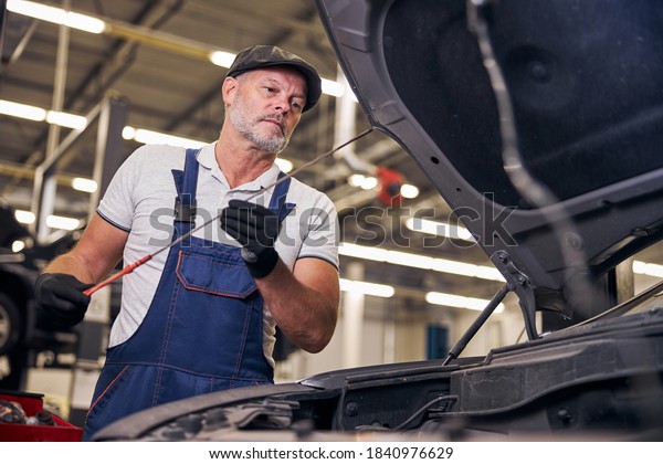 Serious auto mechanic wearing\
work overalls and cap while repairing car in automobile repair\
garage