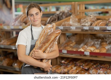 Serious baker standing with fresh bread in a bakery, caucasian young woman standing at the bakery counter and looking at the camera, tired baker with bread in background. copy space