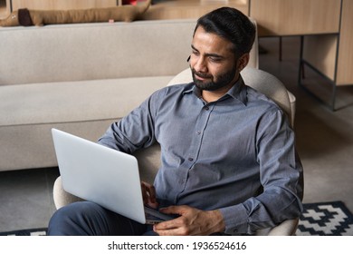 Serious Bearded Indian Business Man Working On Laptop From Home Office Sitting In Chair. Male Indian Entrepreneur Using Computer Remote Studying, Browsing Web, Having Virtual Meeting, Watching Webinar