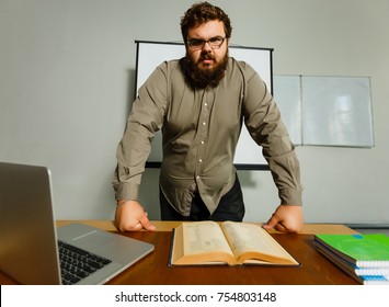 Serious Bearded Professor In Plaid Shirt And Tweed Vest, Wearing Glasses, Shows Something On School Black Board With His Folding Pointer