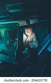 Serious Bearded Senior Man Looking At The Rear View Mirror While Driving His Four-Wheel Vehicle At Night.