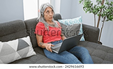 Serious and beautiful middle age woman, comfortably sitting on her cozy sofa at home, immersed in a mature and engrossing conversation through an online video call on her trusty gadget