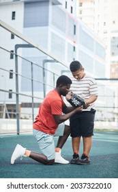 Serious Black Baseball Coach Being Down On One Knee And Adjusting Glove On Boys Hand At Sports Ground