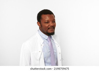 Serious Black Doctor Man With Small Beard In White Coat Bright Shirt Isolated On White Background. Adult Black African American Physician Therapist Portrait, Attractive Practitioner Family Doctor