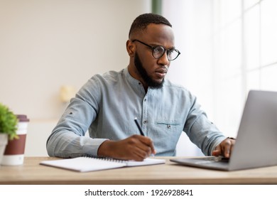 Serious Black Man Writing Business Report At Laptop Or Filling Tax Form At Workplace Sitting In Modern Office. Paperwork, Entrepreneurship Occupation And Career Concept