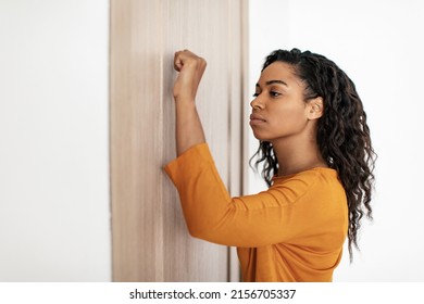 Serious Black Millennial Lady Knocking At The Door Of Apartment Standing In Doorway At Home. Real Estate Offer And Apartment Ownership Concept. Side View Shot