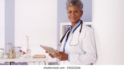 Serious Black Senior Doctor Working On Tablet In Office