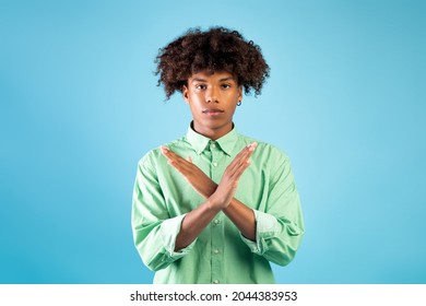 Serious Black Teen Guy Showing Stop Or No Gesture Over Blue Studio Background, Free Space. Annoyed African American Guy Crossing Hands, Dislike Or Deny Something