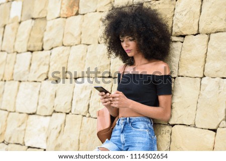 Serious black woman with afro hair looking at her smart phone outdoors.