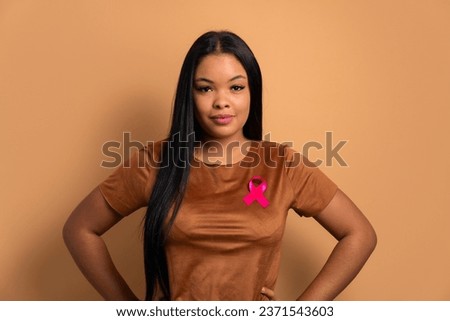 serious black woman showing pink ribbon in beige background. breast cancer, awareness concept.