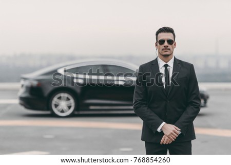 serious bodyguard standing with sunglasses and security earpiece on helipad 