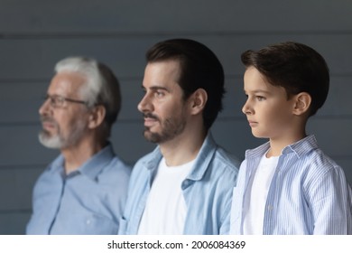 Serious boy, his father and grandpa standing together in row, looking forward. Portrait of three male generations, preschool child, young man, older pensioner. Family relations, heredity concept