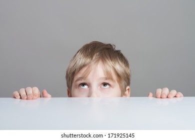 Serious Boy Looking Up From Behind The Table, Close-up Shot