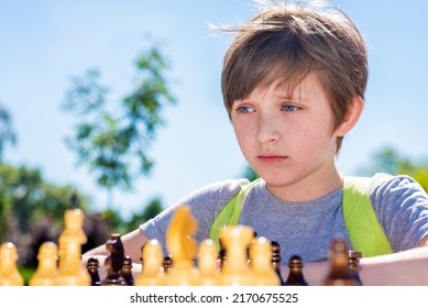 Serious Boy Playing Chess Outside In The Summer