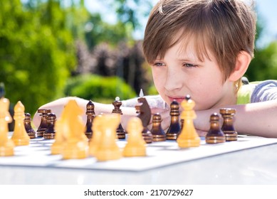 Serious Boy Playing Chess Outside In The Summer