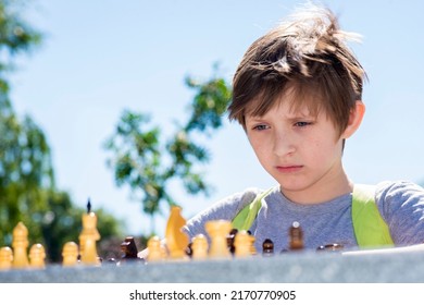 Serious Boy Playing Chess Outside In The Summer