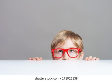 Serious Boy In Red-framed Eyeglasses Looking Up From Behind The Table, Close-up Shot