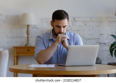 Serious brooding confused man sit at table staring at laptop screen learning new software, get e-mail, reading received information looks concerned or puzzled. Business issue, search solution concept