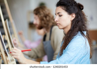 Serious brunette woman sketching with pencil at lesson of painting in school of arts - Powered by Shutterstock