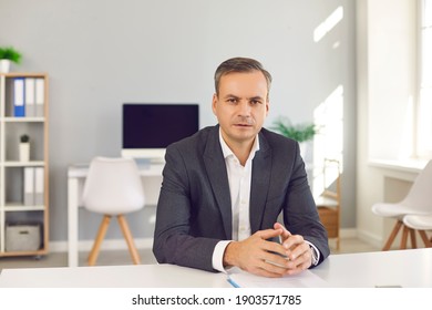 Serious Business Man Sitting At Office Desk, Looking At Camera And Listening To You. Portrait Of HR Manager, CEO, Bank Advisor, Financial Consultant, Political Expert, Teacher Or University Professor