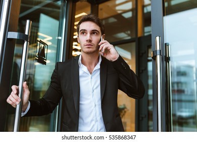 Serious Business Man In Suit Talking On Phone In Office And Holding The Door. From Below Image.