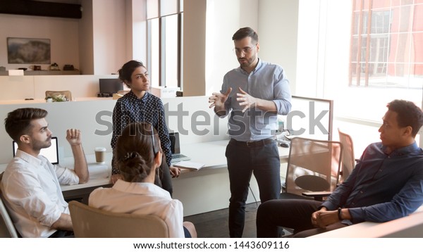 Serious business man team leader coach mentor\
talk to diverse business people in office explain strategy at\
corporate group meeting, multiethnic staff listen to boss instruct\
interns at briefing