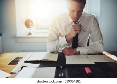 Serious business man working on documents looking concentrated with briefcase and phone on the table - Shutterstock ID 339364181