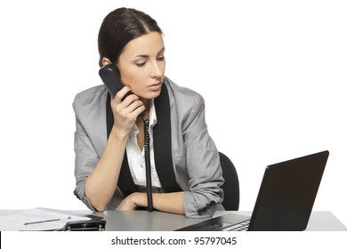 Serious Business Woman Looking At Laptop Screen While Talking On The Phone At Her Work Desk, Isolated On White Background