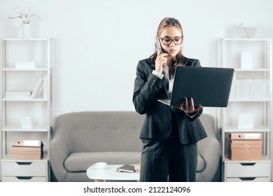 Serious Business Woman In Suit Making Phone Call. Business Woman Freelancer Using Laptop Typing On Pc Notebook, Surfing Internet In Office.