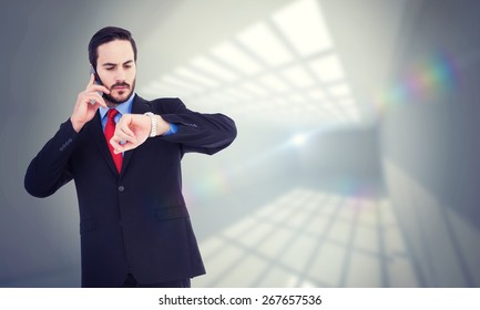 Serious businessman checking the time while on the phone against room with windows at ceiling