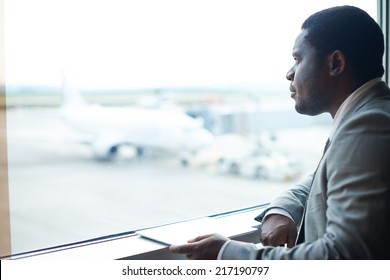 Serious businessman with digital tablet looking through window in airport - Powered by Shutterstock