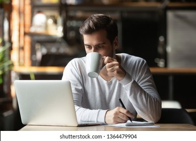 Serious Businessman First Guest In Cafe Sitting In Coffee House Holding Pen Make Notes Use Notepad Looking At Computer Screen Reading Today Online News Starting Day Drinking Hot Coffee In The Morning