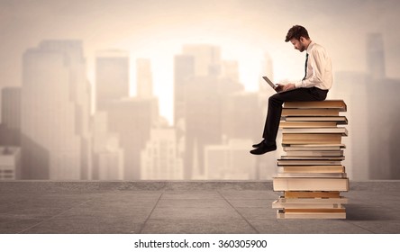 A serious businessman with laptop tablet in elegant suit sitting on a stack of books in front of cityscape