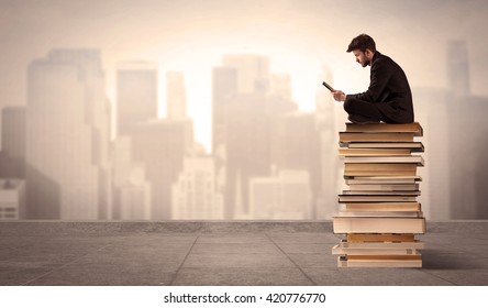 A Serious Businessman With Laptop Tablet In Elegant Suit Sitting On A Stack Of Books In Front Of Cityscape