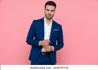 Serious businessman looking forward while wearing blue suit and standing on pink studio background