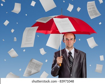 Serious businessman with red umbrella under falling documents