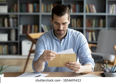 Serious businessman sit at workplace office desk holding envelope take out letter feels interested read business news, got invitation, learns bank statement information. Postal correspondence concept - Shutterstock ID 1854695413