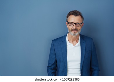 Serious businessman wearing glasses staring intently at the camera with a focused expression against a blue studio background with copy space - Powered by Shutterstock