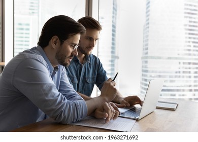 Serious businessmen sit at desk in office look at laptop screen discuss financial business paperwork together. Focused male employees colleagues work on computer, think in group. Teamwork concept. - Shutterstock ID 1963271692