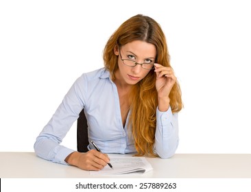 Serious Businesswoman With Glasses Skeptically Looking At You Sitting At Office Desk Isolated On White Background. Human Face Expression, Body Language, Attitude