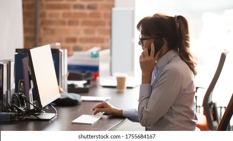 Serious businesswoman in glasses using computer, looking at screen, secretary consulting client customer on phone in office, searching information, solving business problem online, horizontal photo