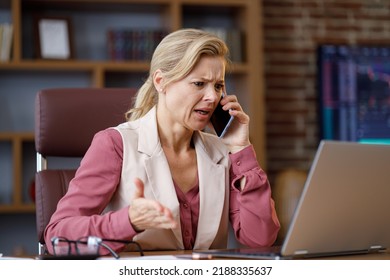 Serious Businesswoman Having Unpleasant Phone Conversation Working On Laptop Sitting At Office. Female Trader Listening Bad News, Feels Desperate, Receive Bad Information About Monetary Investments